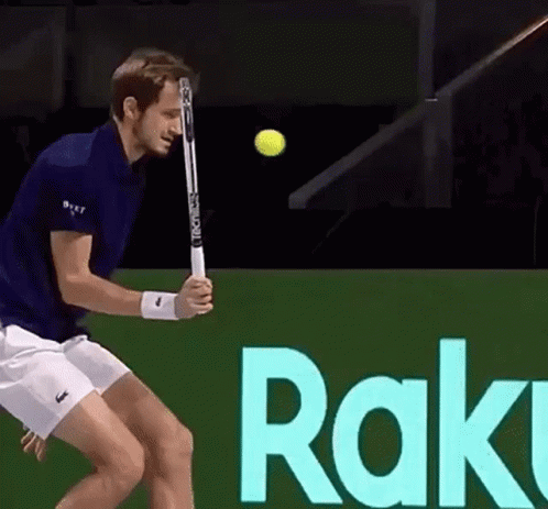 A Man Is Swinging A Tennis Racket At A Tennis Ball In Front Of A Sign That Says Rak GIF