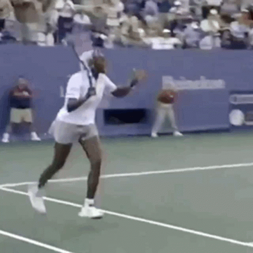 A Man Is Swinging A Tennis Racket On A Tennis Court In Front Of A Crowd . GIF