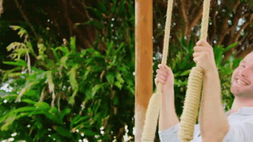 A Man Is Swinging On A Rope Swing Outside GIF