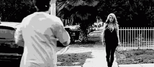 A Man Is Taking A Picture Of A Woman Walking Down The Street . GIF