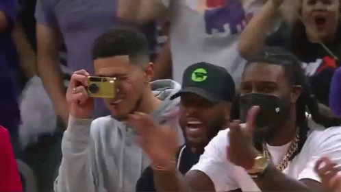 A Man Is Taking A Picture Of Another Man With A Camera While Sitting In The Stands . GIF