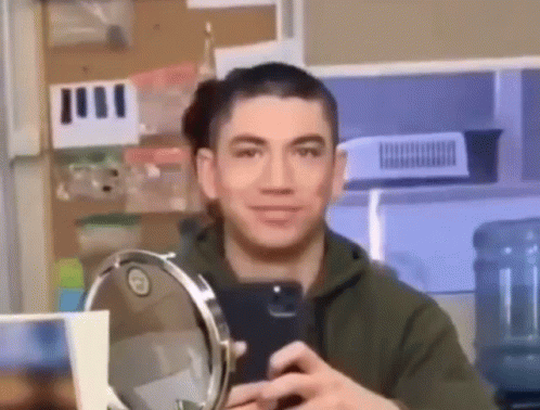 A Man Is Taking A Picture Of Himself In A Mirror . GIF