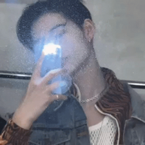A Man Is Taking A Picture Of Himself In A Mirror With His Phone . GIF