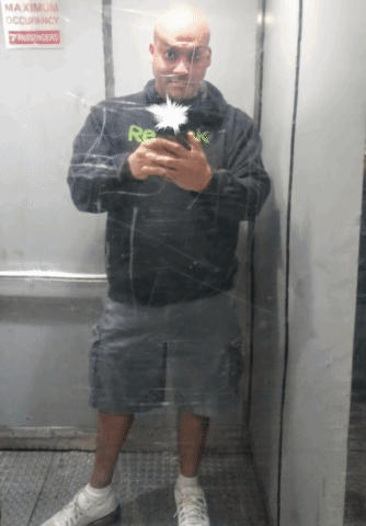 A Man Is Taking A Picture Of Himself In An Elevator With A Sign That Says Maximum Occupancy 7 Passengers GIF
