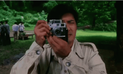 A Man Is Taking A Picture With A Camera In The Park . GIF