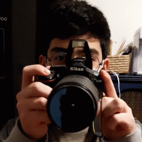 A Man Is Taking A Picture With A Camera That Says Nikon On It GIF