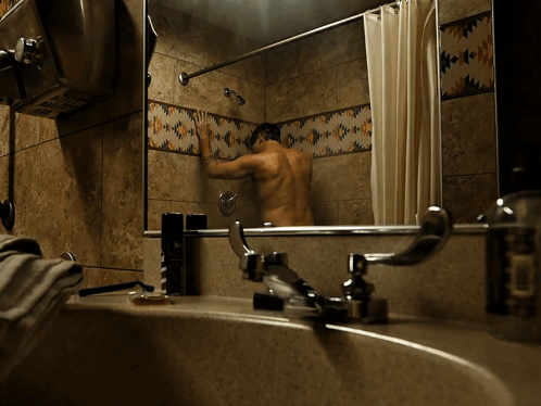 A Man Is Taking A Shower In A Bathroom With Native American Tiles GIF
