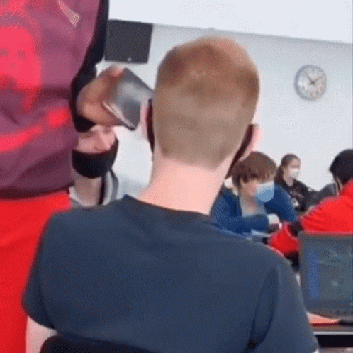 A Man Is Talking On A Cell Phone In A Classroom While Sitting At A Desk . GIF
