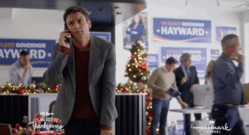 A Man Is Talking On A Cell Phone In Front Of A Hallmark Channel Ad For Hayward . GIF