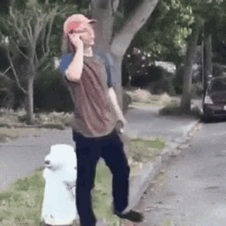 A Man Is Talking On A Cell Phone While Standing Next To A Fire Hydrant On The Side Of The Road . GIF