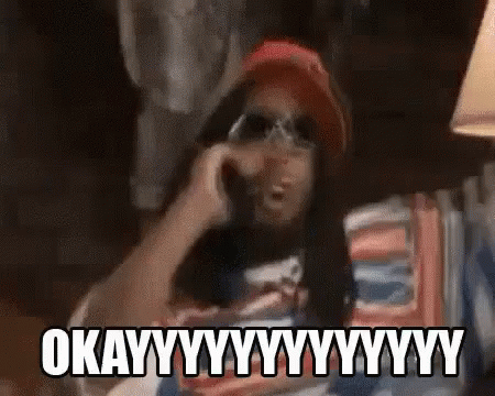 A Man Is Talking On A Cell Phone While Wearing Sunglasses And A Hat . GIF