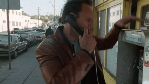 A Man Is Talking On A Pay Phone With A Sign That Says ' Pay Here And Get Paid ' On It GIF
