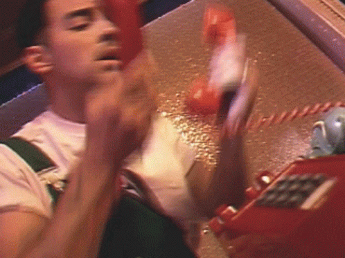 A Man Is Talking On A Red Telephone With His Hand Up GIF