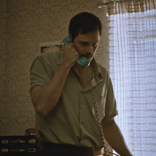 A Man Is Talking On A Telephone In Front Of A Window GIF