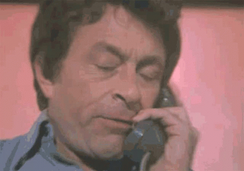 A Man Is Talking On A Telephone With His Eyes Closed And His Mouth Open . GIF
