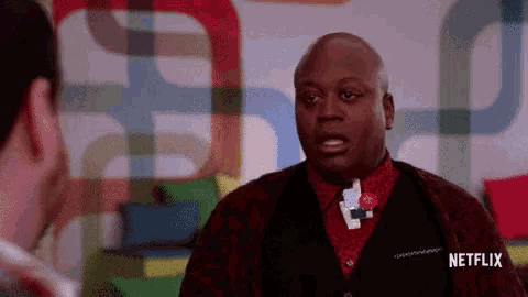 A Man Is Talking To Another Man In Front Of A Colorful Wall . GIF