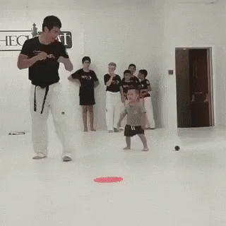 A Man Is Teaching A Child How To Kick A Ball In A Karate Class . GIF