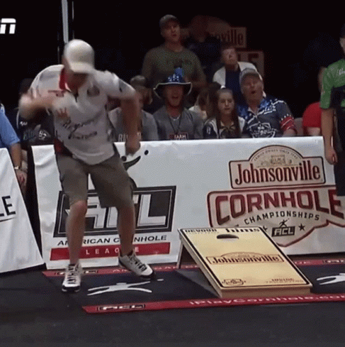 A Man Is Throwing A Frisbee In Front Of A Johnsonville Cornhole Sign GIF