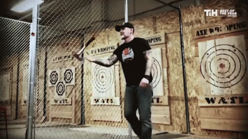 A Man Is Throwing An Axe In Front Of A Wall That Says " Axe Throwing " GIF