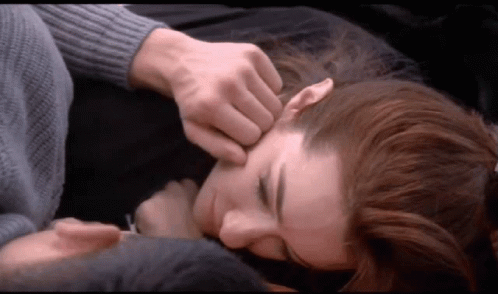 A Man Is Touching A Woman 'S Forehead While Laying On A Bed GIF