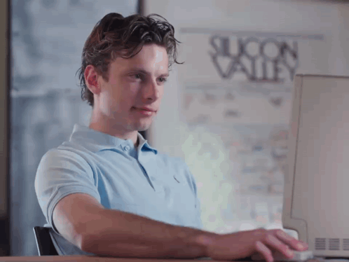 A Man Is Typing On A Computer In Front Of A Silicon Valley Poster GIF