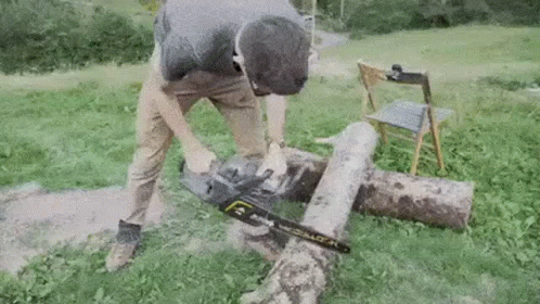 A Man Is Using A Chainsaw To Cut A Log . GIF