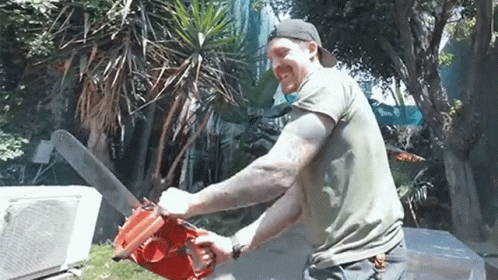 A Man Is Using A Chainsaw To Cut A Tree In A Yard . GIF