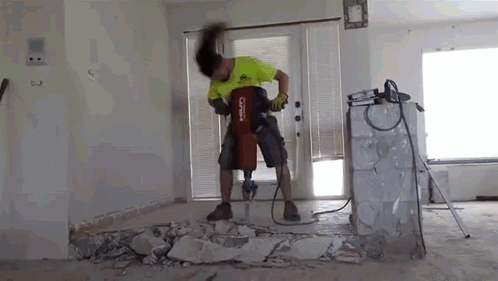 A Man Is Using A Hammer To Break A Wall In A Living Room . GIF