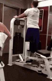 A Man Is Using A Machine In A Gym To Do Squats . GIF