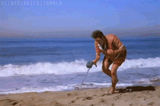 A Man Is Using A Metal Detector To Search For Something On The Beach . GIF