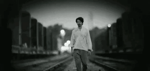 A Man Is Walking Along Train Tracks In A Black And White Photo . GIF
