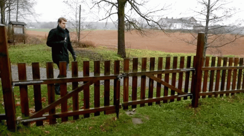 A Man Is Walking Behind A Wooden Fence In A Field GIF