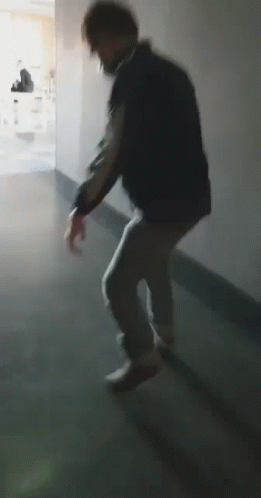 A Man Is Walking Down A Hallway In A Dark Room . GIF