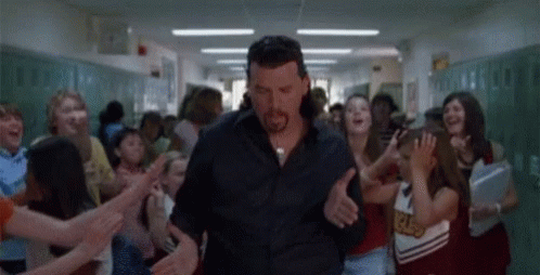 A Man Is Walking Down A Hallway Surrounded By Cheerleaders . GIF