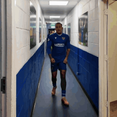 A Man Is Walking Down A Hallway Wearing A Blue Shirt That Says Mandy GIF