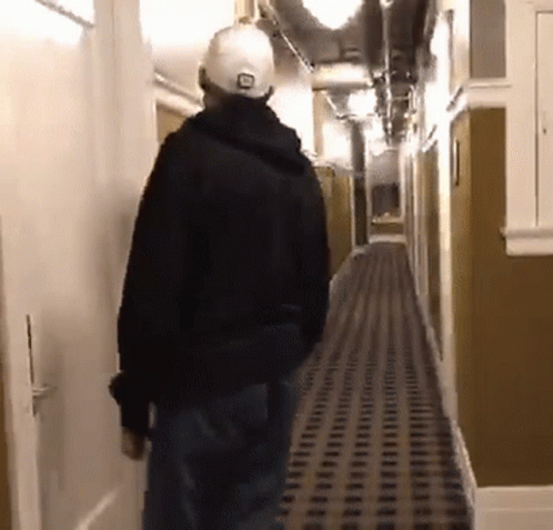 A Man Is Walking Down A Hallway Wearing A Hat That Says Lg On It GIF