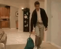 A Man Is Walking Down A Hallway With A Backpack And A Suitcase . GIF