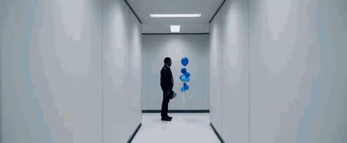 a man is walking down a hallway with a blue bottle in his hand .