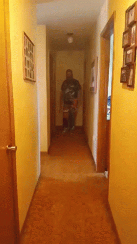 A Man Is Walking Down A Hallway With Pictures On The Walls GIF