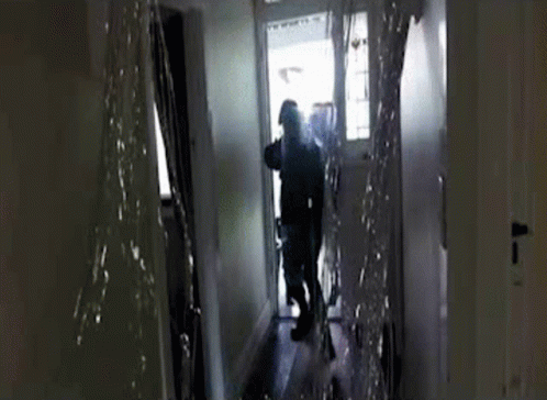 A Man Is Walking Down A Hallway With Water Coming Out Of The Ceiling . GIF