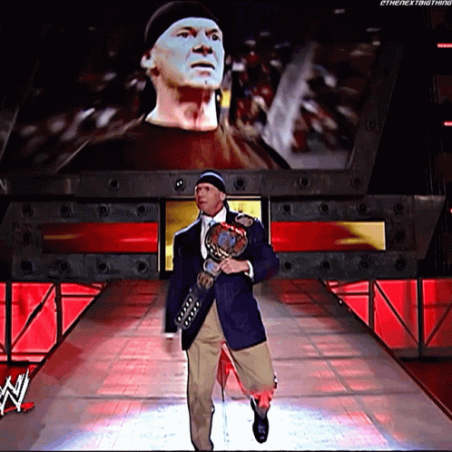 A Man Is Walking Down A Ramp Holding A Wrestling Trophy GIF
