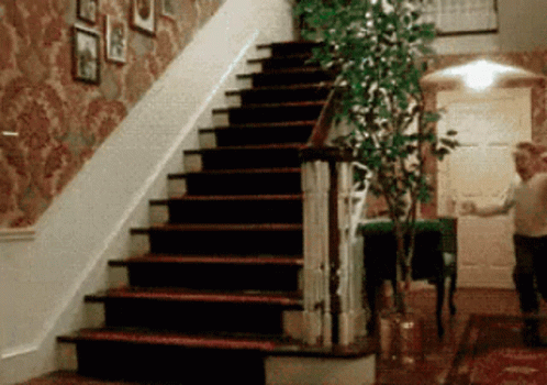 A Man Is Walking Down A Set Of Stairs In A Hallway GIF