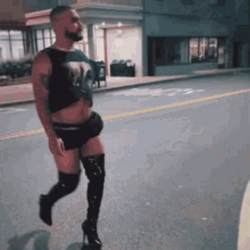 A Man Is Walking Down The Street Wearing Thigh High Boots GIF