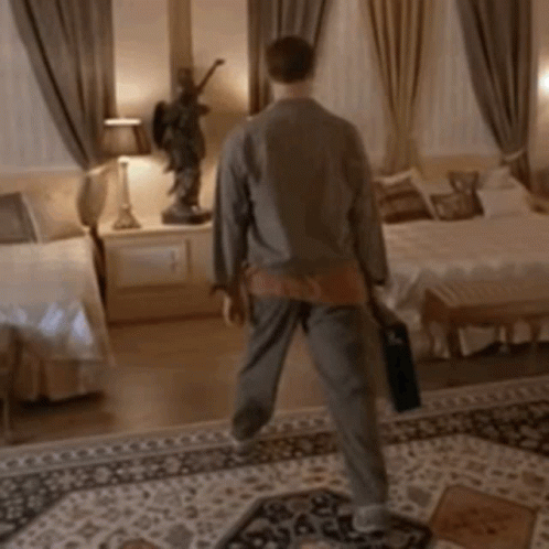 A Man Is Walking In A Bedroom With A Statue Of An Angel On The Wall GIF