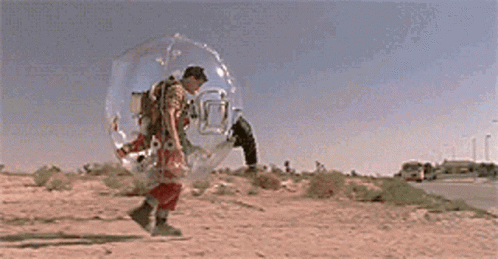 A Man Is Walking In A Clear Bubble On The Side Of A Road . GIF