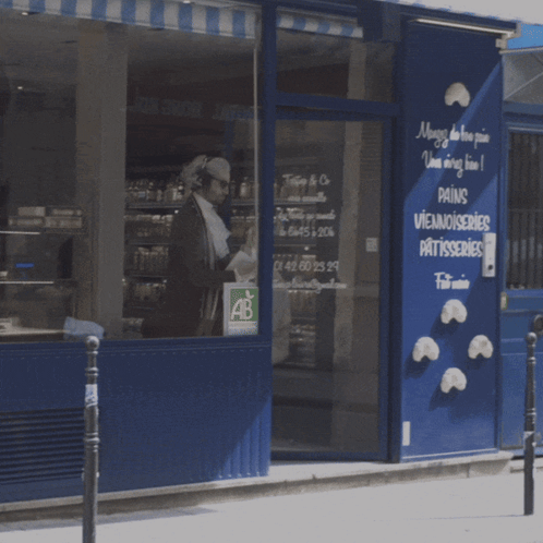 A Man Is Walking In Front Of A Store That Sells Pains Viennoiseries Patisseries GIF