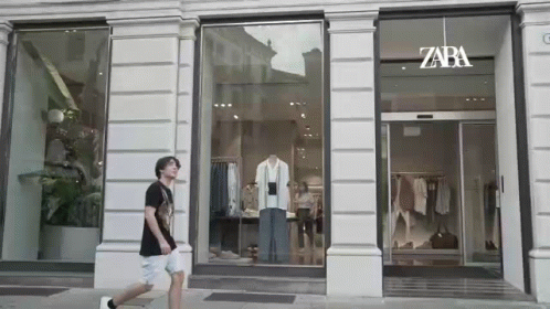 A Man Is Walking In Front Of A Store With A Mannequin In The Window . GIF