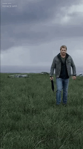A Man Is Walking Through A Grassy Field With An Umbrella GIF