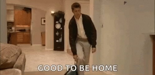 A Man Is Walking Through A Living Room Carrying A Suitcase And A Vacuum Cleaner . GIF