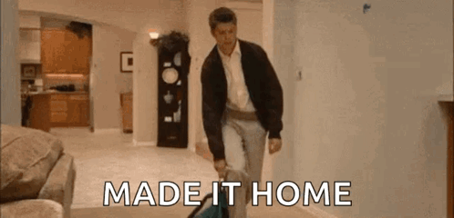 A Man Is Walking Through A Living Room Carrying A Suitcase And The Words `` Made It Home '' . GIF